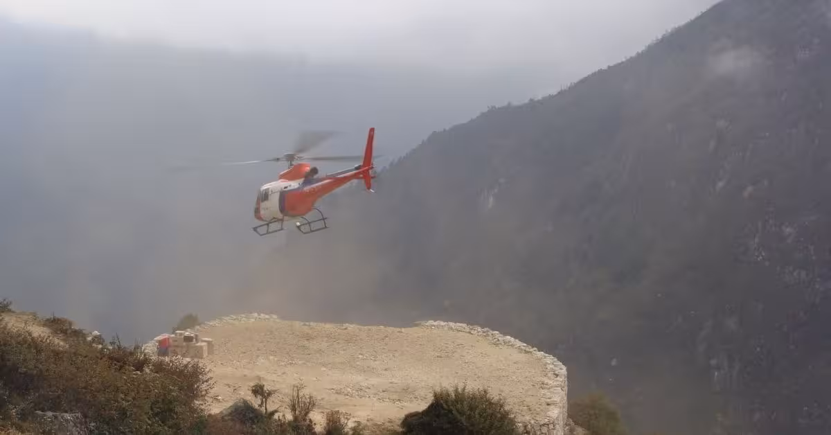 Red and white helicopter taking off from a small helipad on a mountain ridge on Everest Region