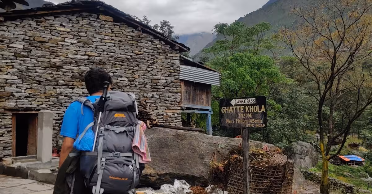 Backpacker passing stone houses near Ghatte Khola on Manaslu route