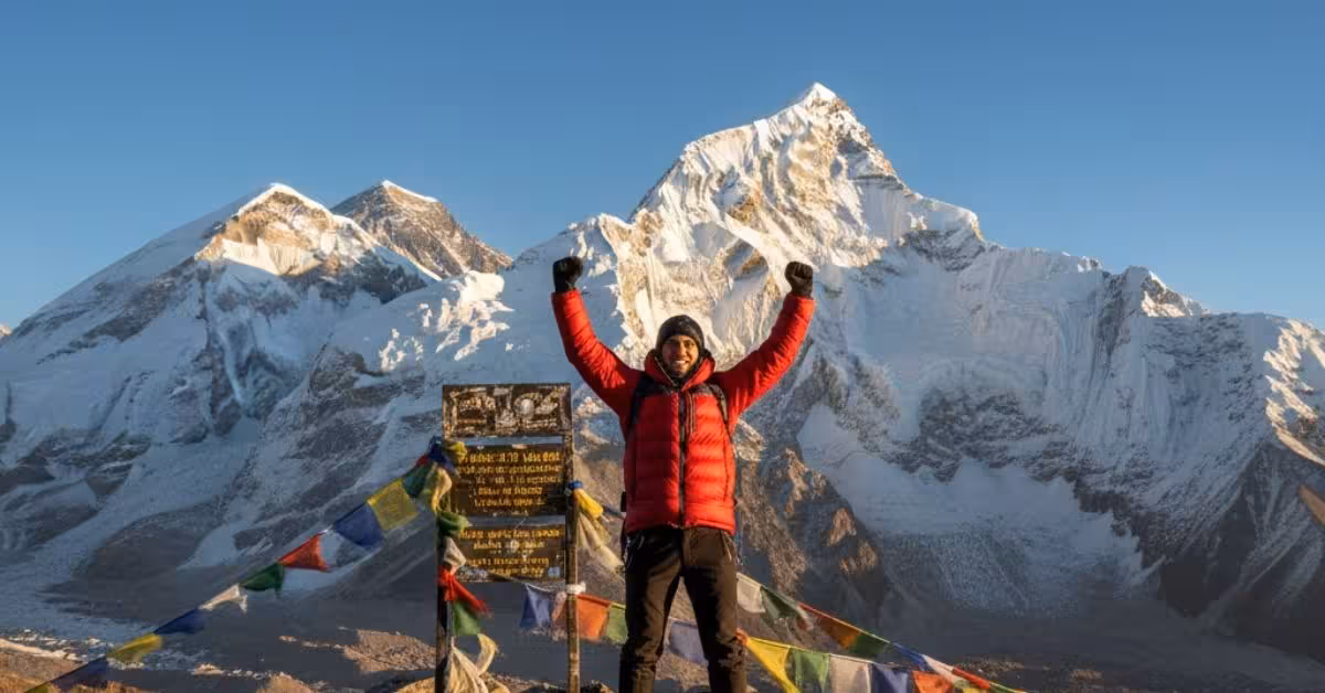 Hiker standing with arms raised at Kala Patthar summit signboard